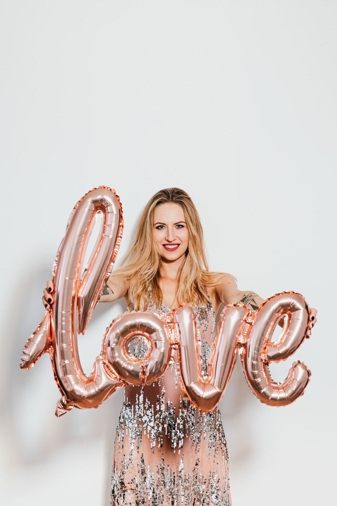 Mujer con vestido de lentejuelas sostiene globos dorados 'love'