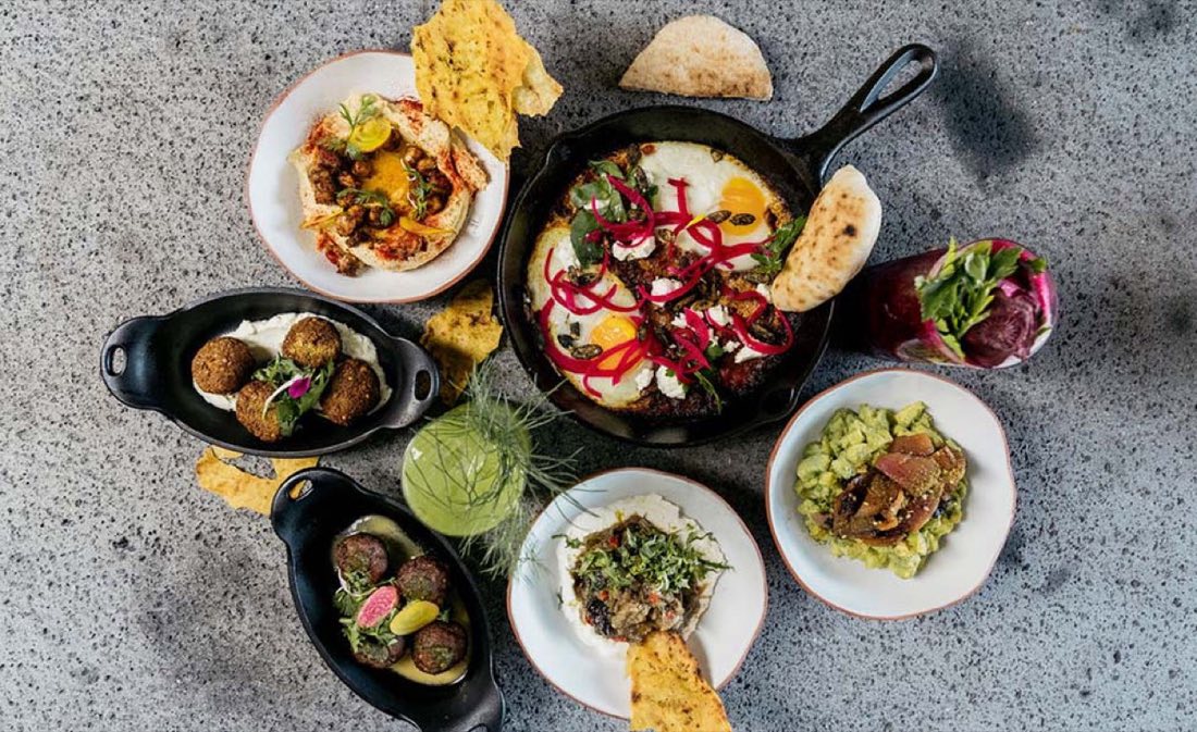 Hummus, falafel y shakshuka sobre mesa de piedra, vista cenital
