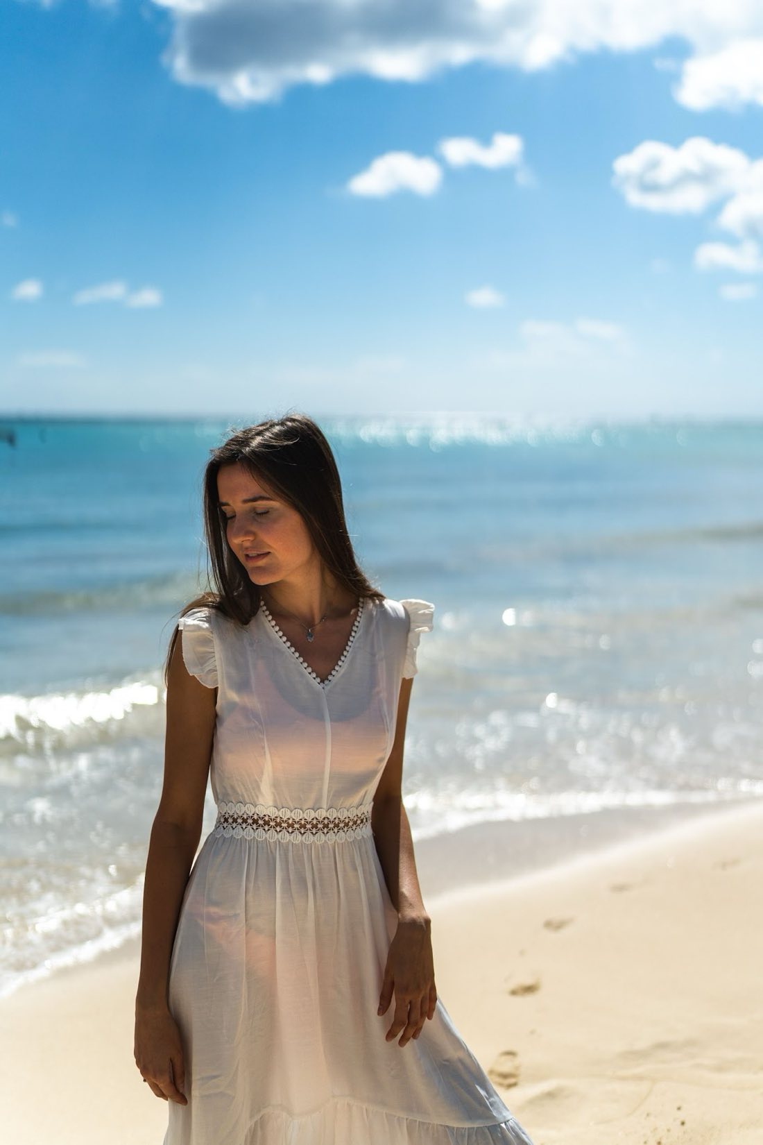 Mujer de vestido blanco camina por la orilla del Caribe