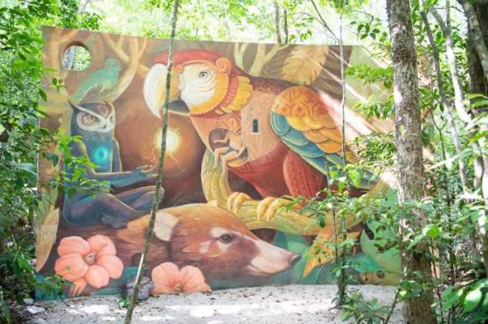 A visitor seated inside a large white egg-shaped sculpture set against a painted mural in the jungle.