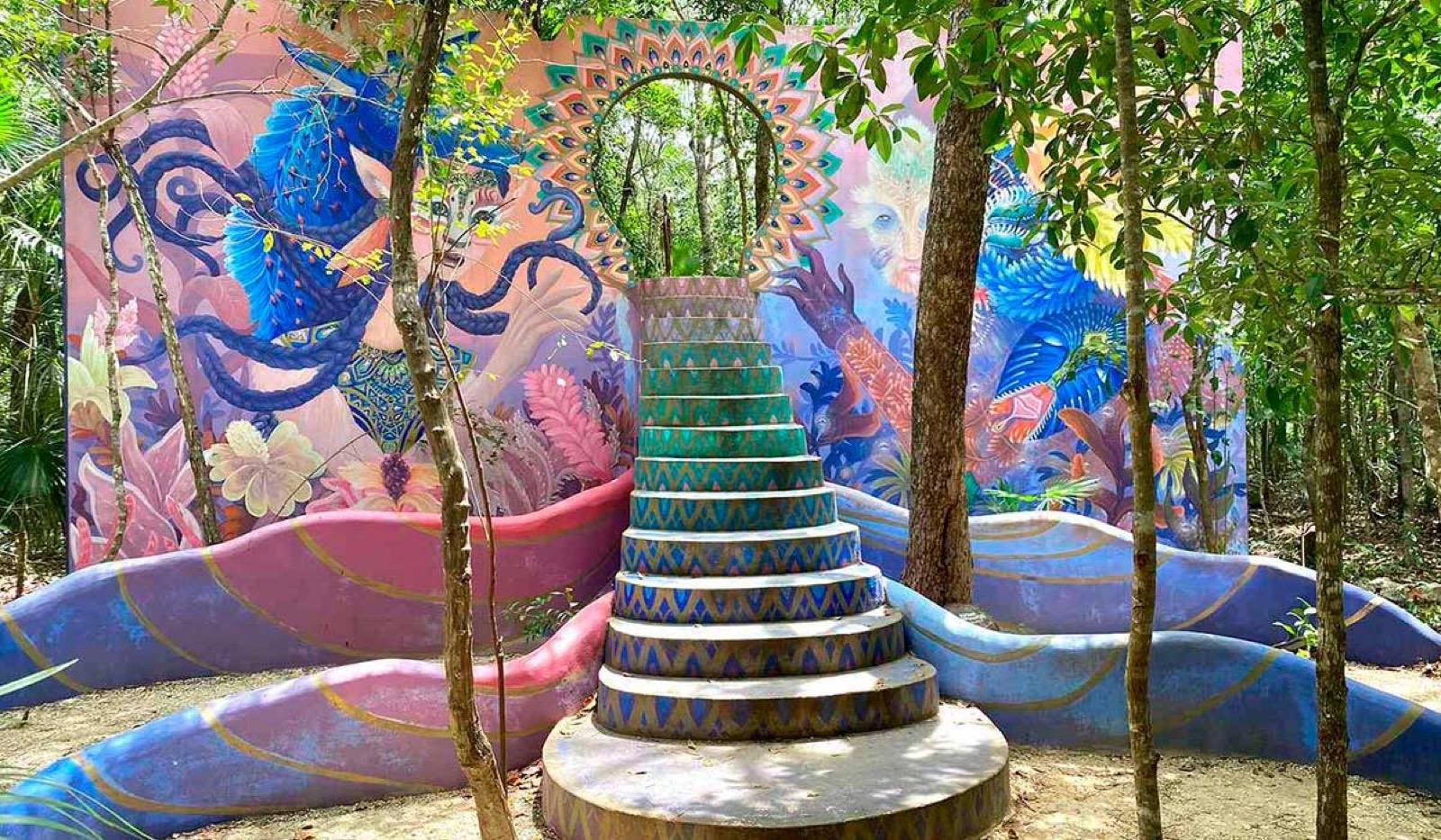 A vivid painted mural and a spiral tiled staircase sculpture among the jungle trees on the Tulum art walk.