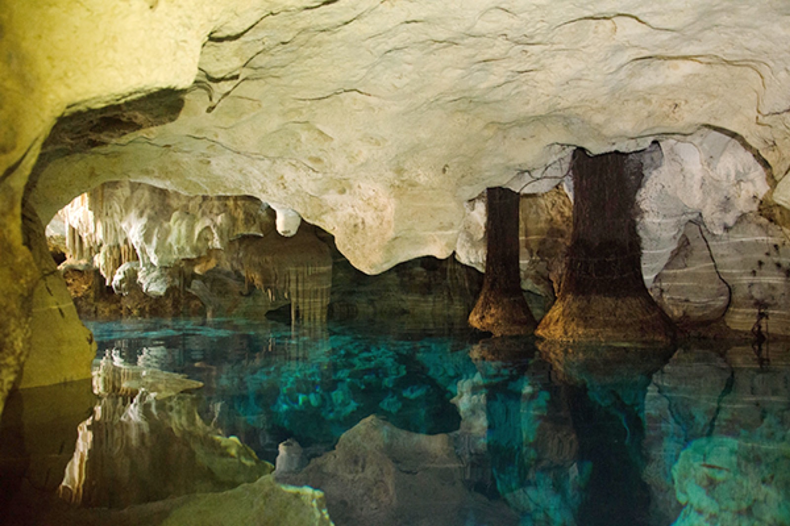 Un cenote de caverna con estalactitas reflejadas en el agua turquesa y serena bajo tierra.