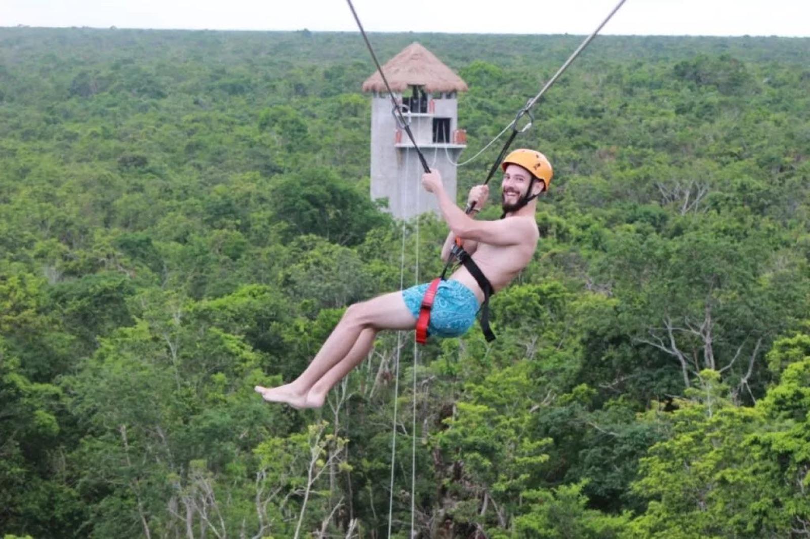 Man ziplining over the jungle canopy with a thatched lookout tower behind him