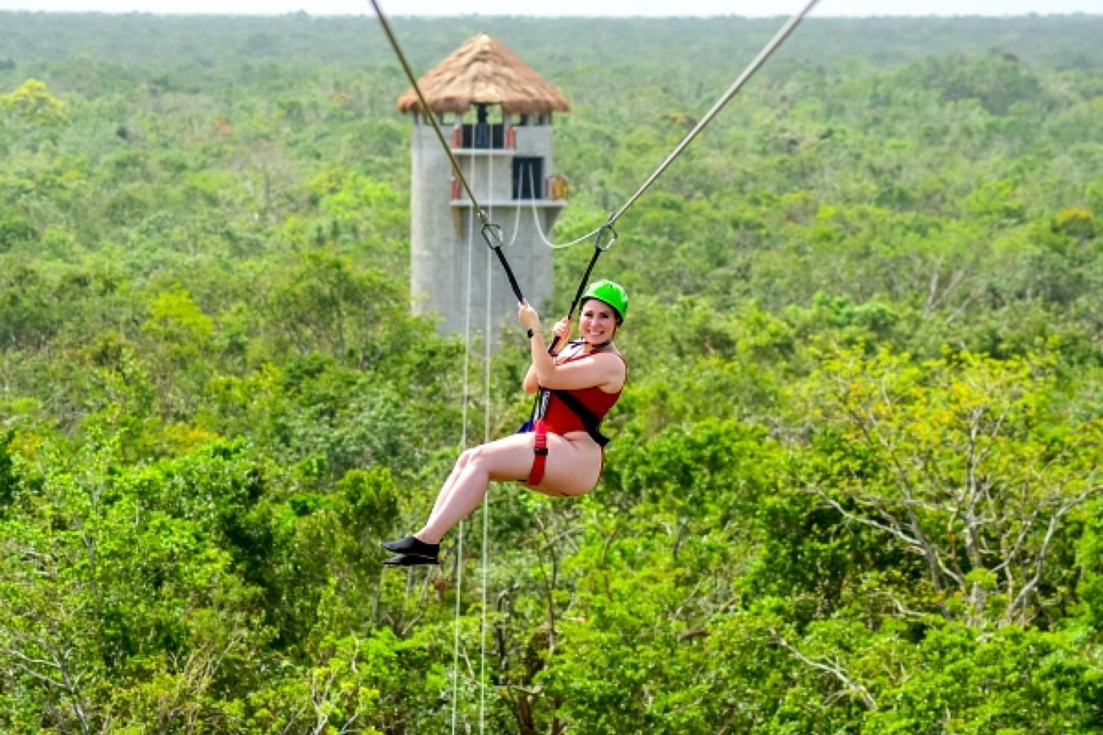 Woman ziplining over the jungle with a lookout tower in the background on a clear day