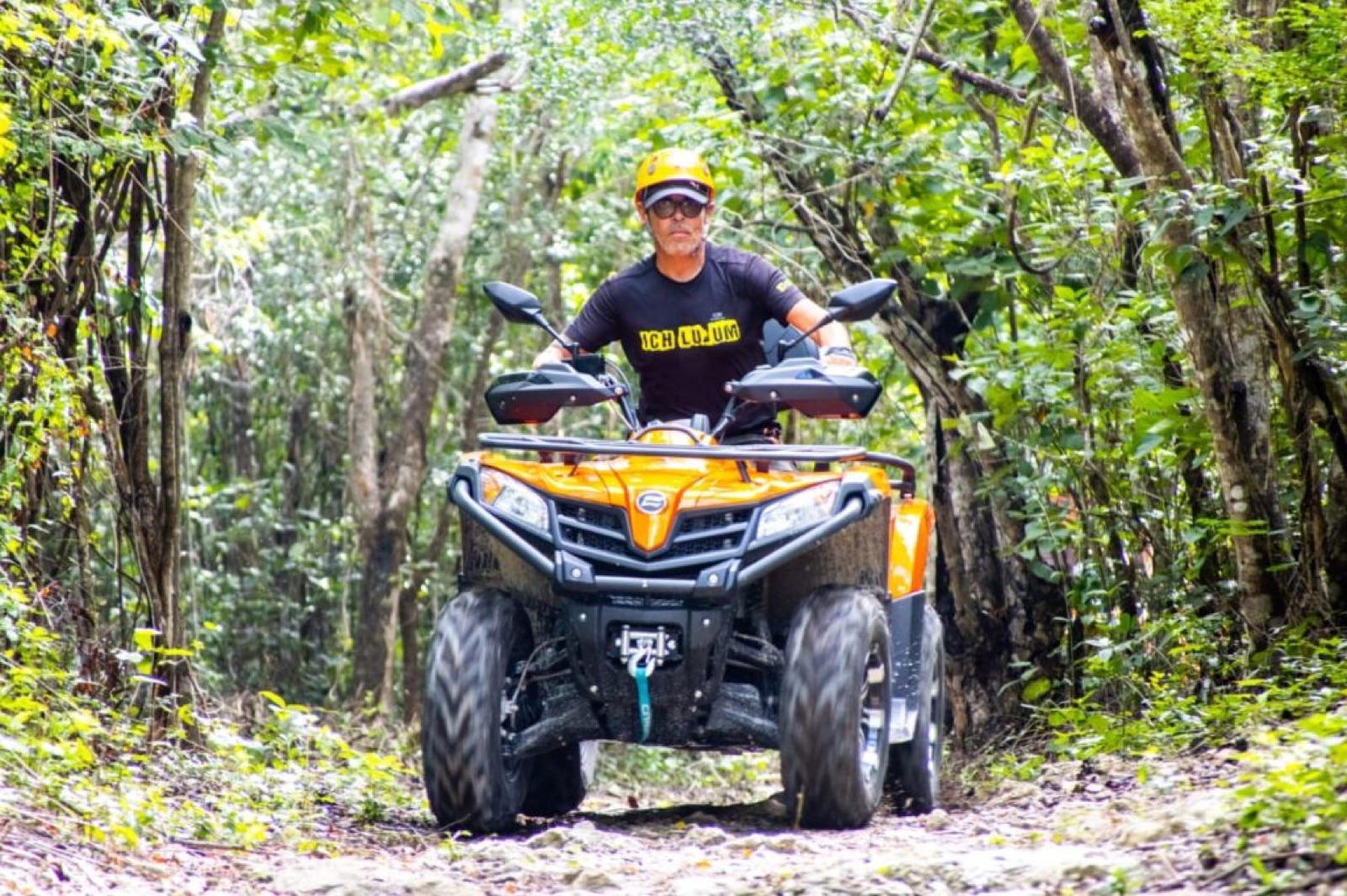 Rider on an orange ATV quad bike on a jungle trail in the Riviera Maya, wearing a helmet on a sunny day