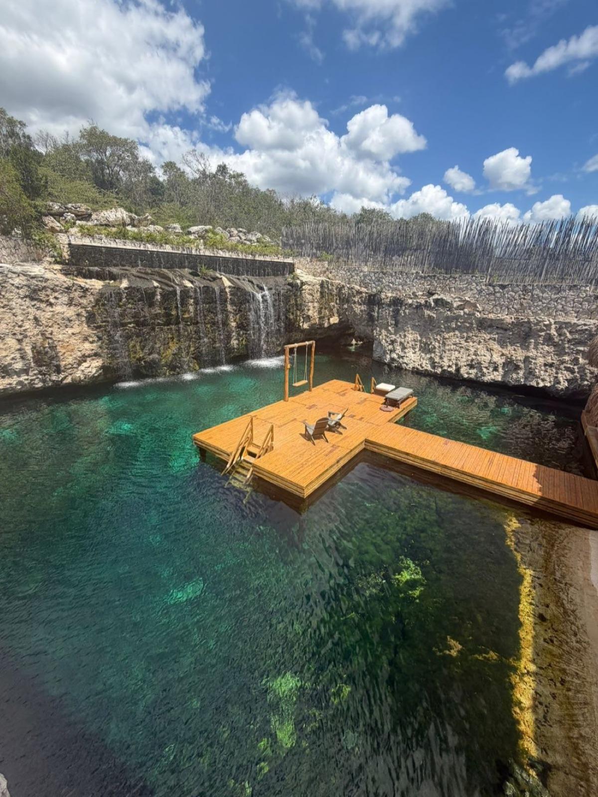 Aerial view of the private cenote, a wooden deck reaching out over clear turquoise water below a stone wall.