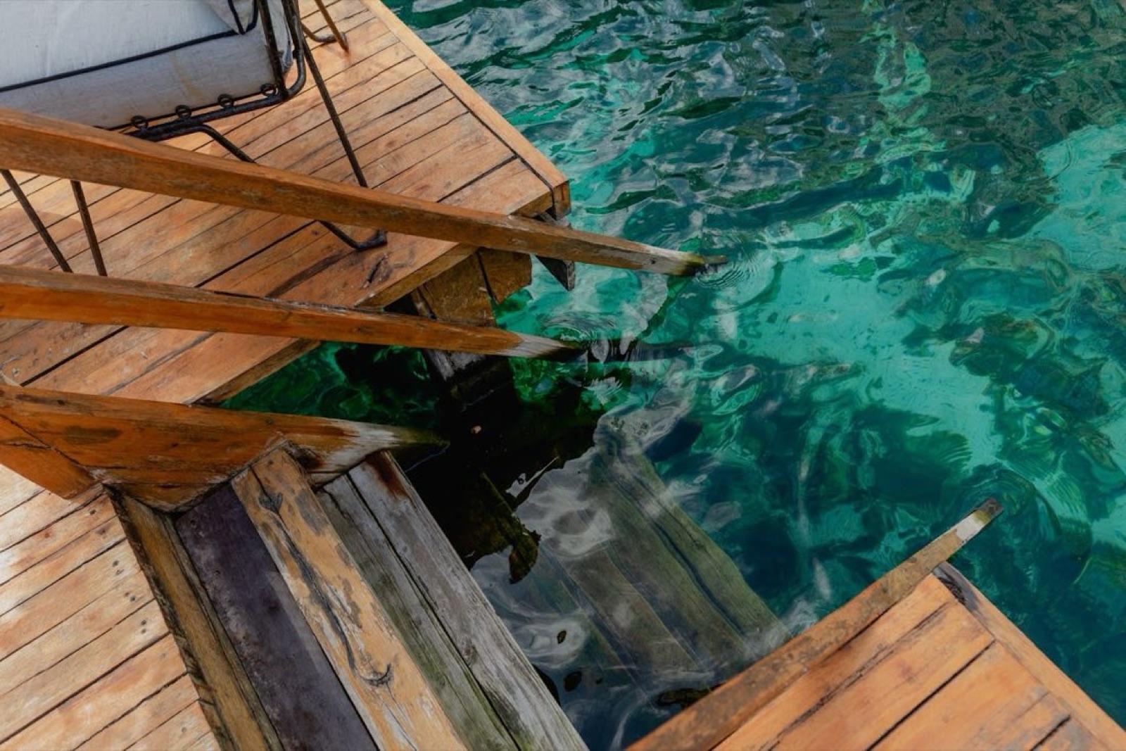 Close-up of the wooden deck steps descending into the clear turquoise cenote water.
