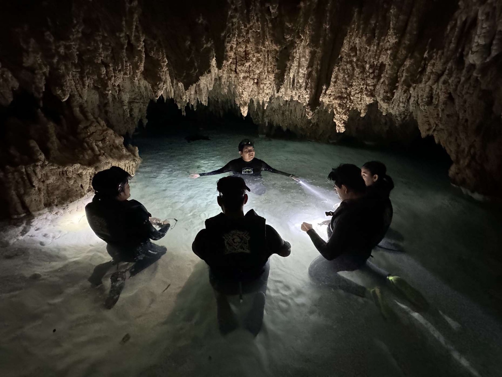 A small group wading through a dark cavern cenote lit by their torches.