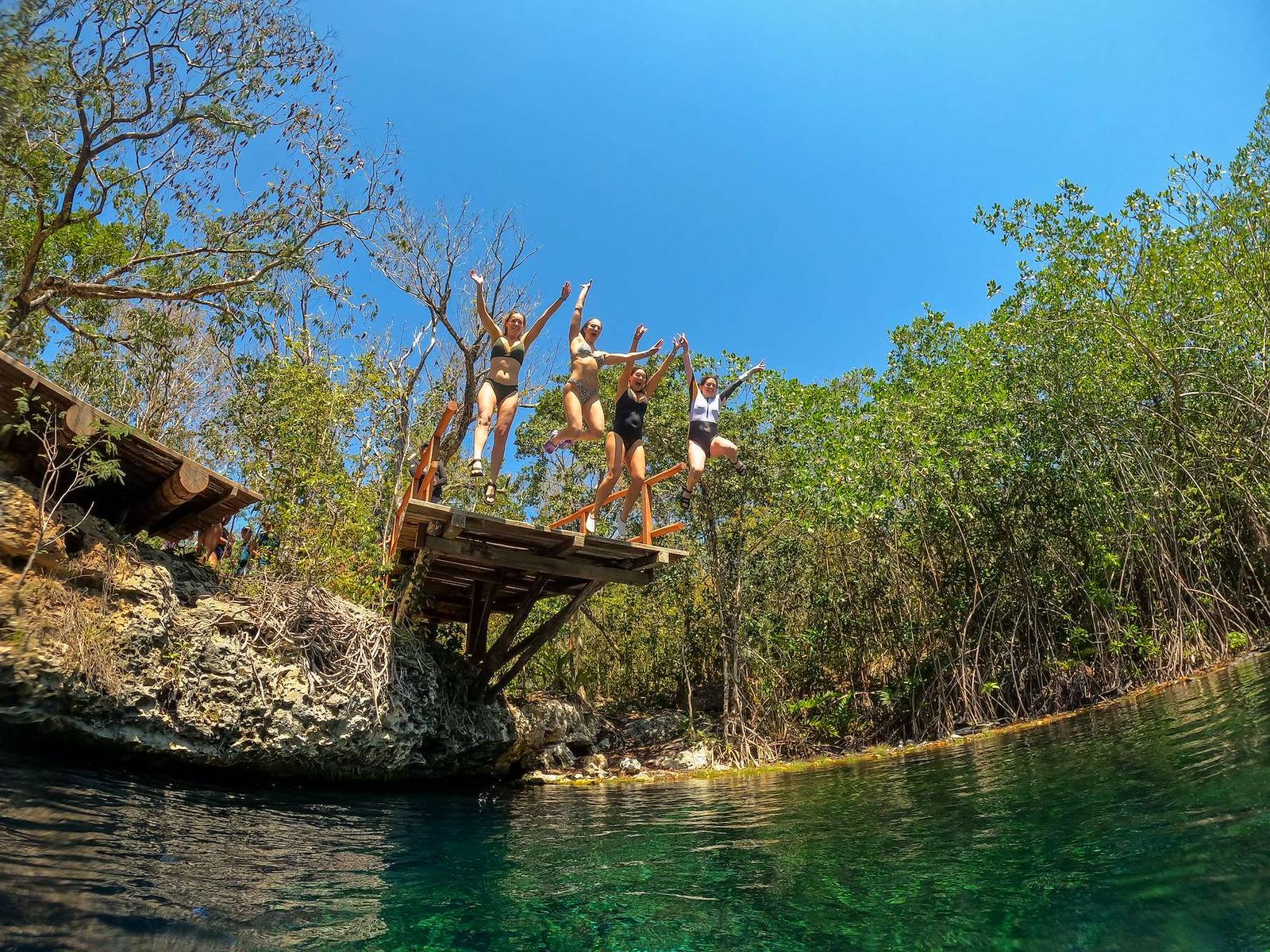 Friends jumping together from a wooden platform into an open cenote