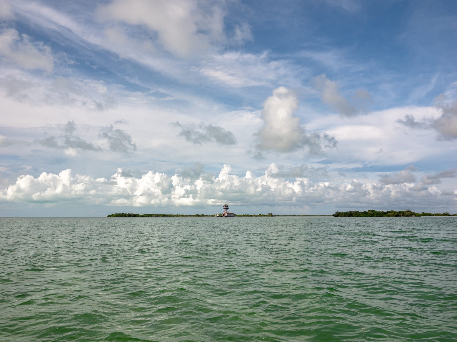 Mar abierto y una línea baja de islotes bajo nubes de verano