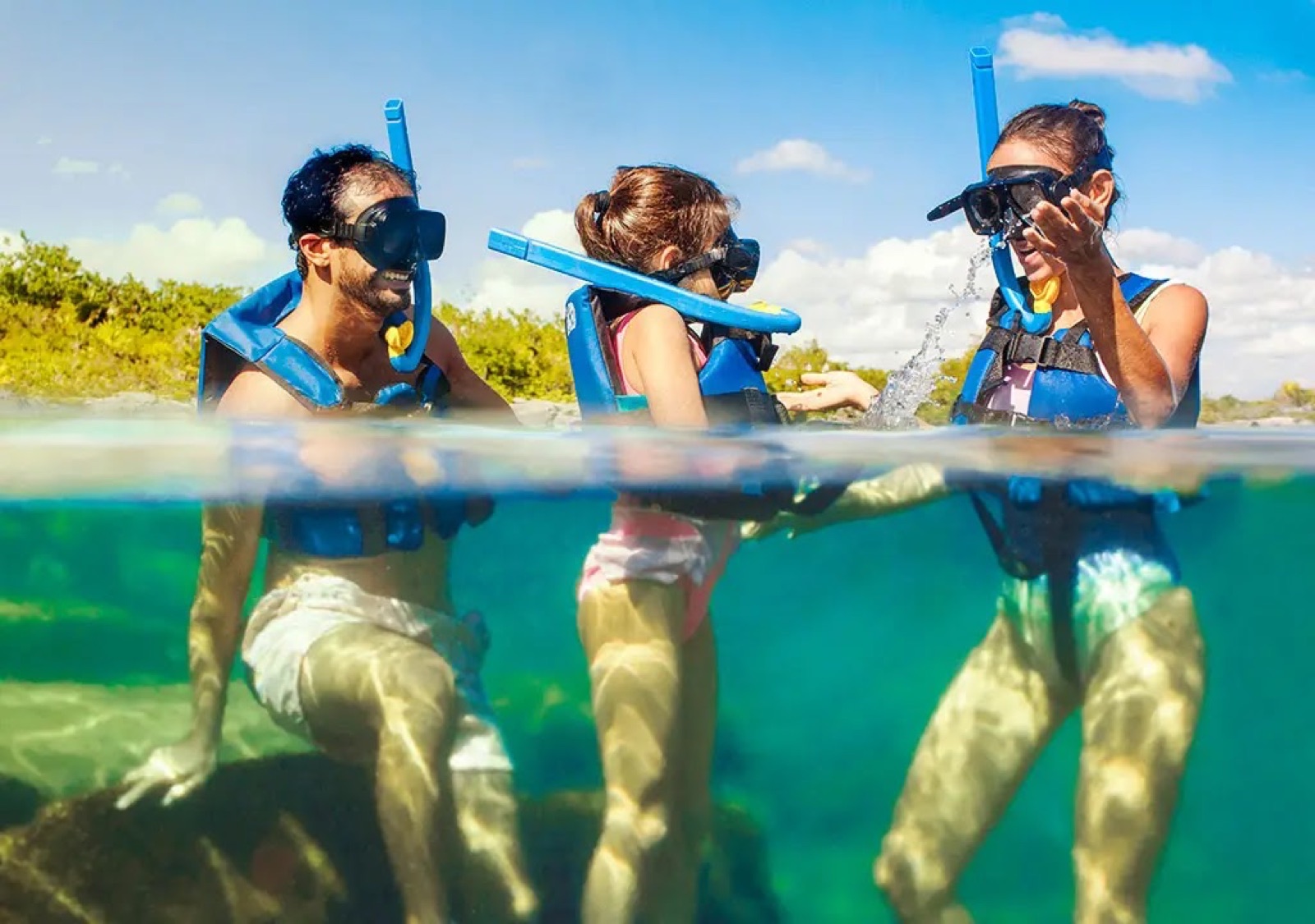 A family snorkeling in the calm Yal-Kú lagoon, half above and half below the clear water.