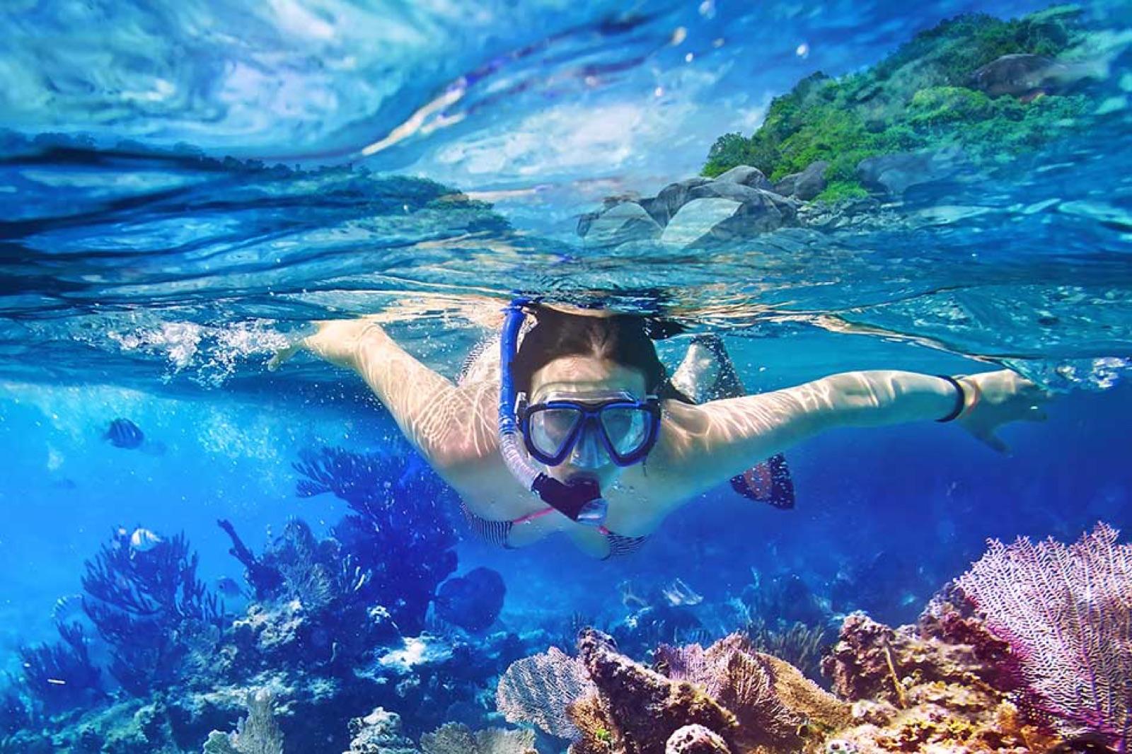 A snorkeler gliding over colorful coral and fish in the clear water of Yal-Kú.