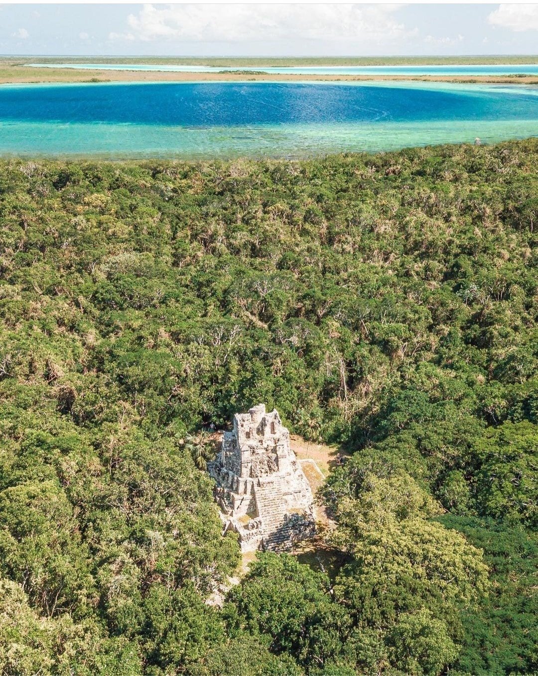 Aerial view of the Muyil pyramid in the jungle, with the lagoon behind
