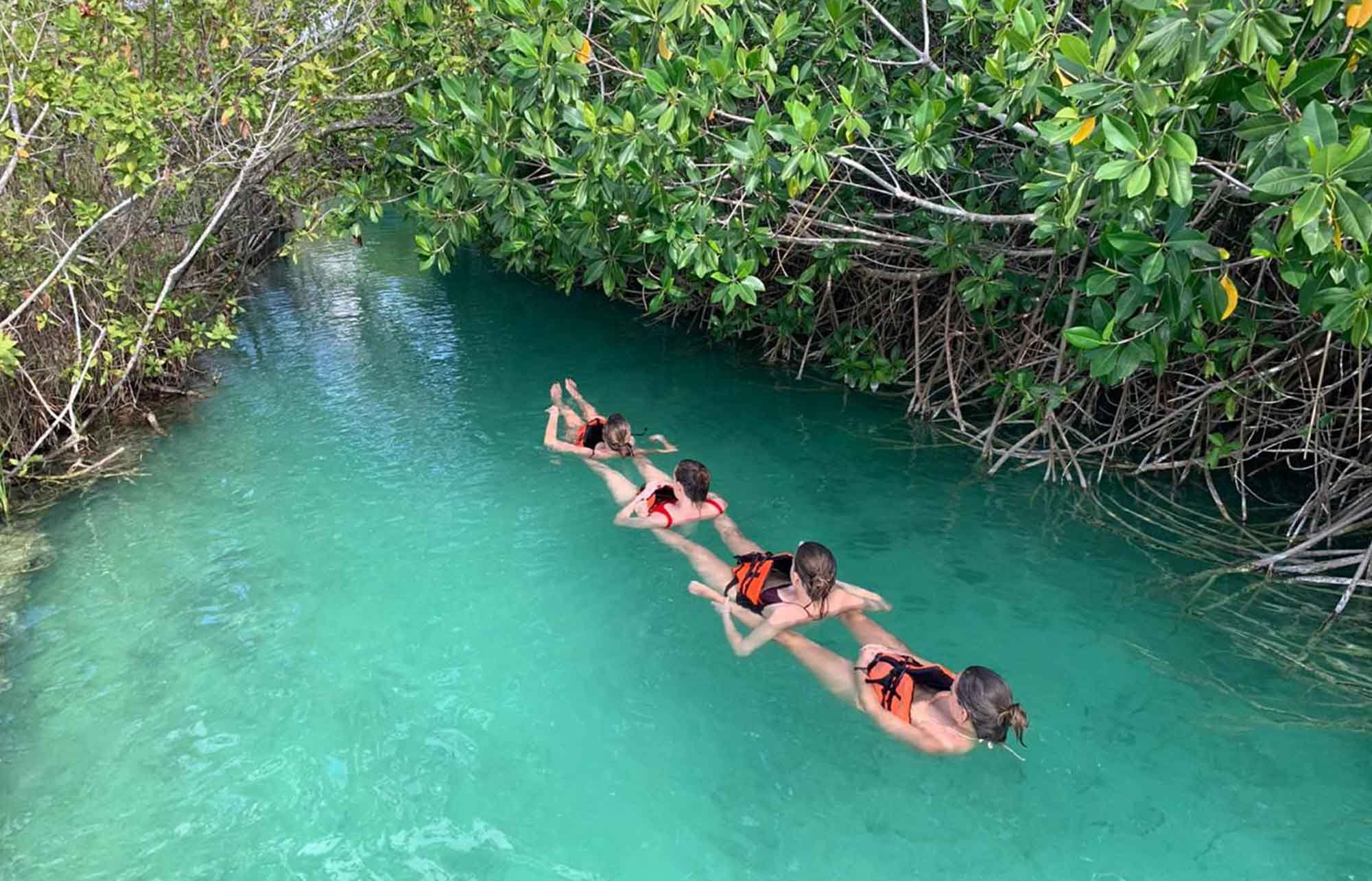 Huéspedes con chaleco flotando por el canal turquesa de Muyil entre manglares.
