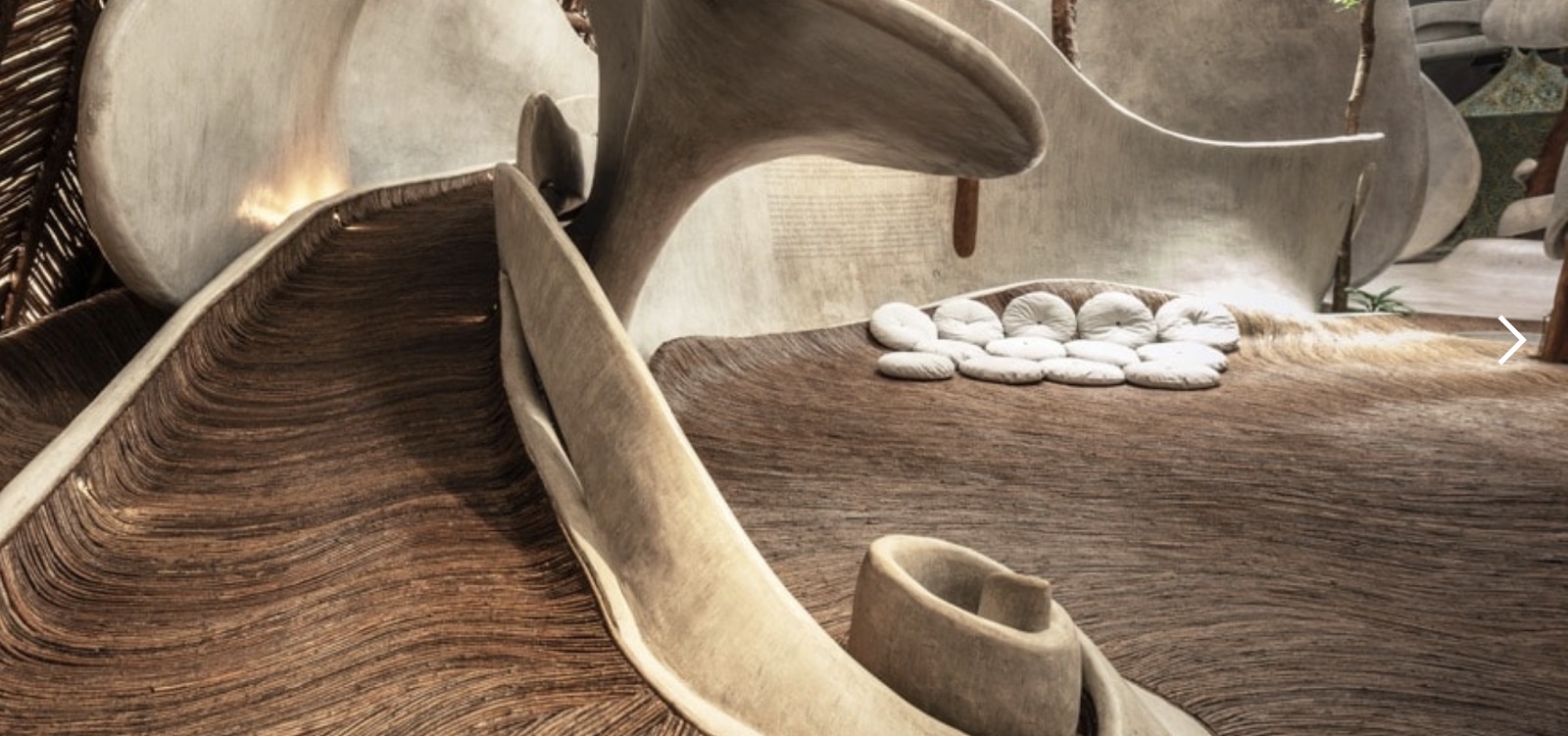 Detail of SFER IK's organic architecture: a woven, polished wood floor curving into white sculptural forms with rounded white pebbles.