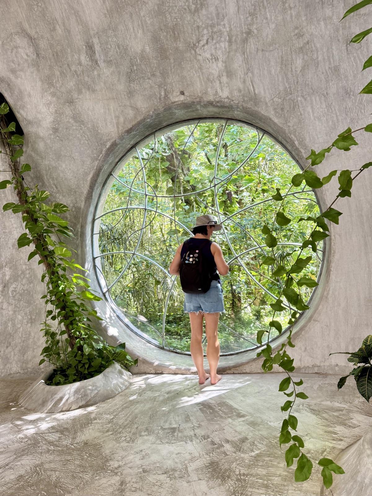 A large round portal window at SFER IK framing the surrounding jungle, with a visitor standing in the opening.