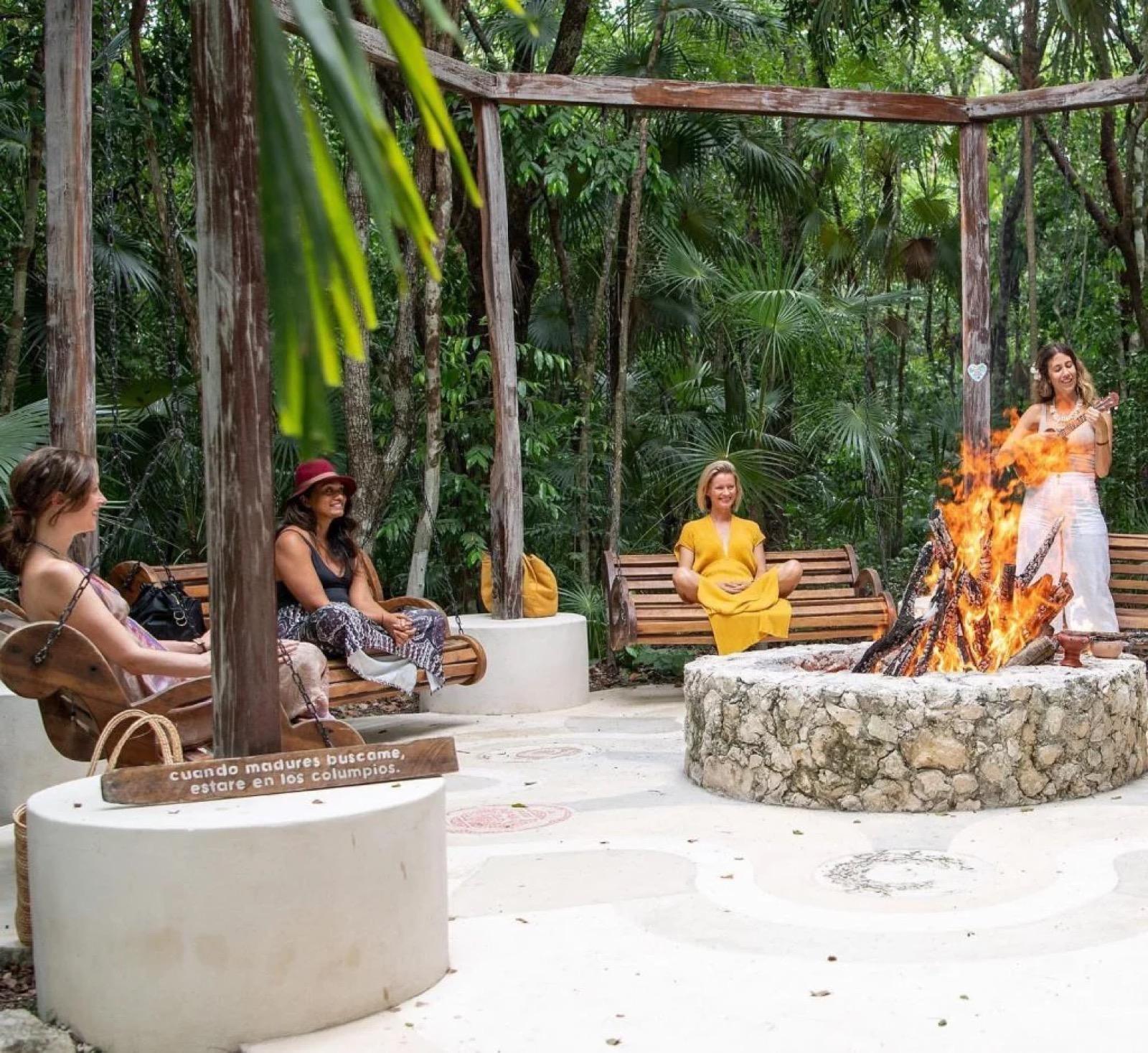 Un grupo sentado en bancos de madera alrededor de una fogata de piedra durante una ceremonia de temazcal en la selva.