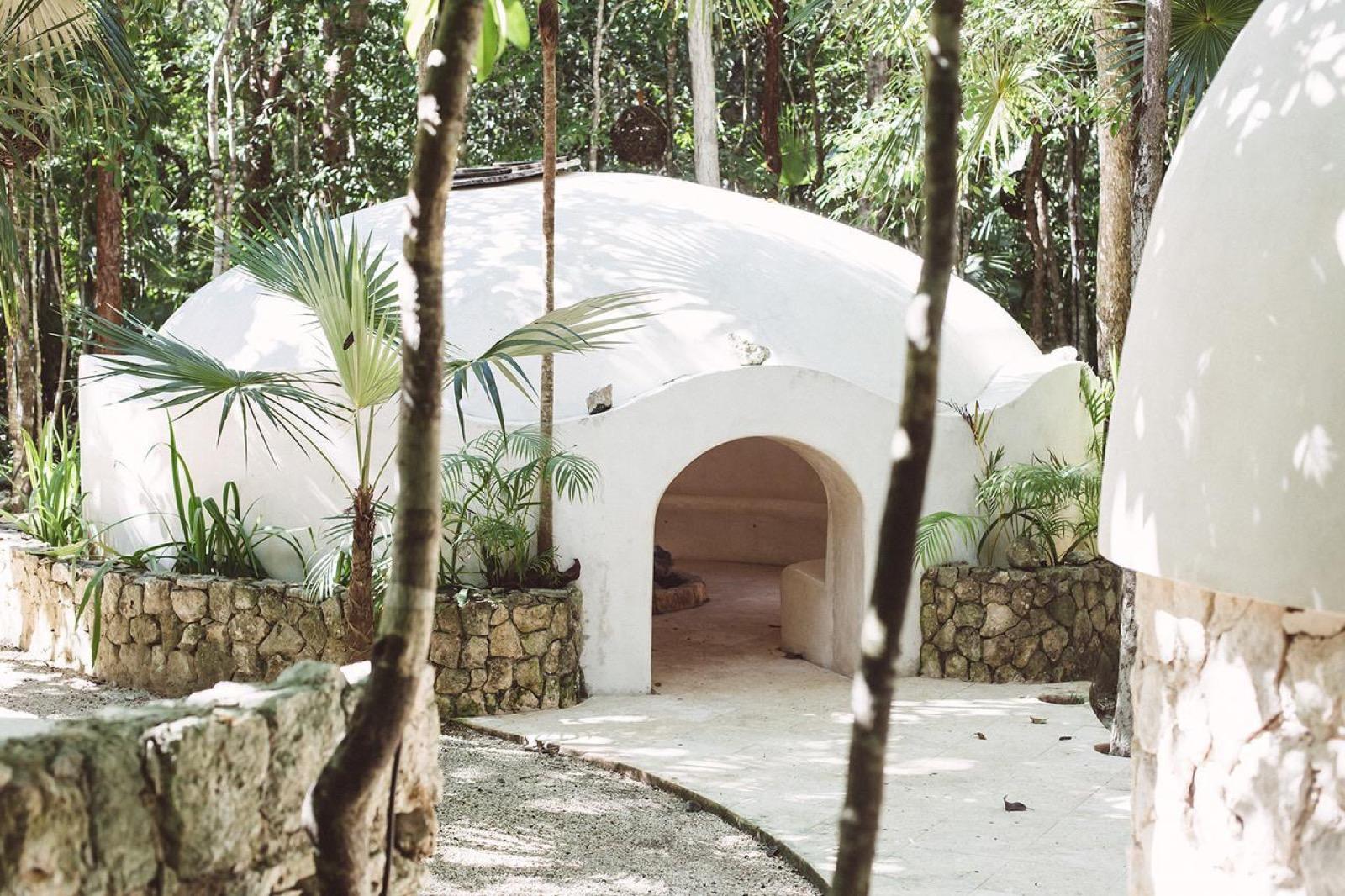 Domo blanco de un temazcal maya con entrada en arco, rodeado de vegetación tropical de la selva.