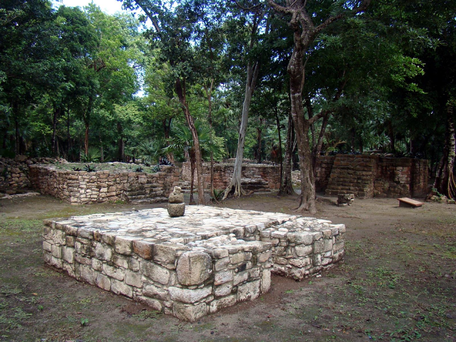 A weathered Maya stone platform standing in a jungle clearing at the Xel-Há archaeological zone.