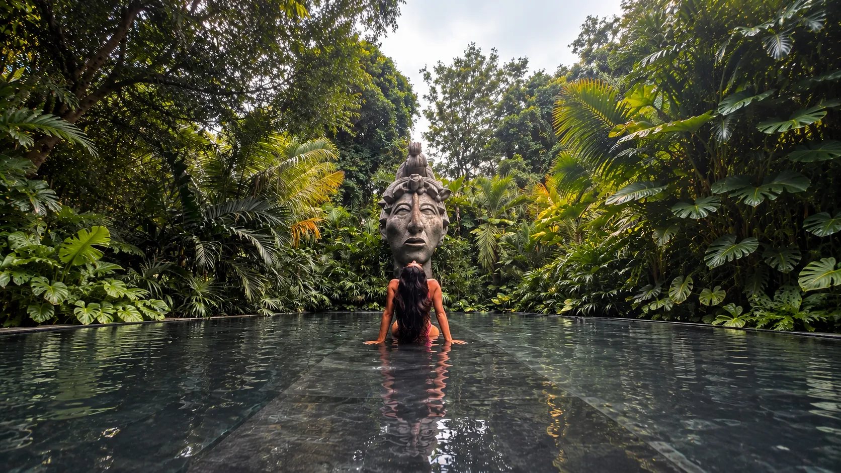 A guest in a jungle pool facing a carved Maya stone head