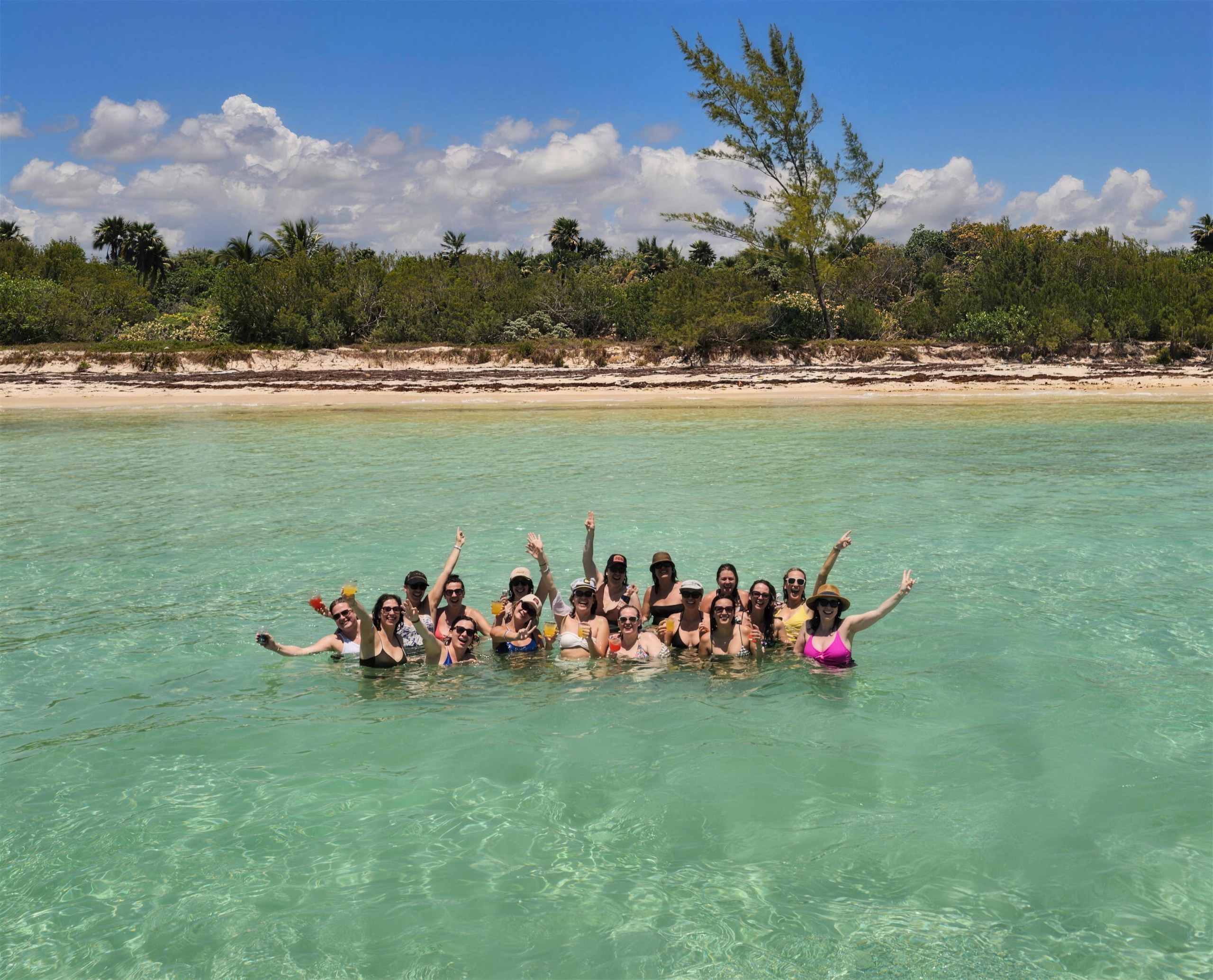 The whole group standing in the turquoise shallows with their arms up