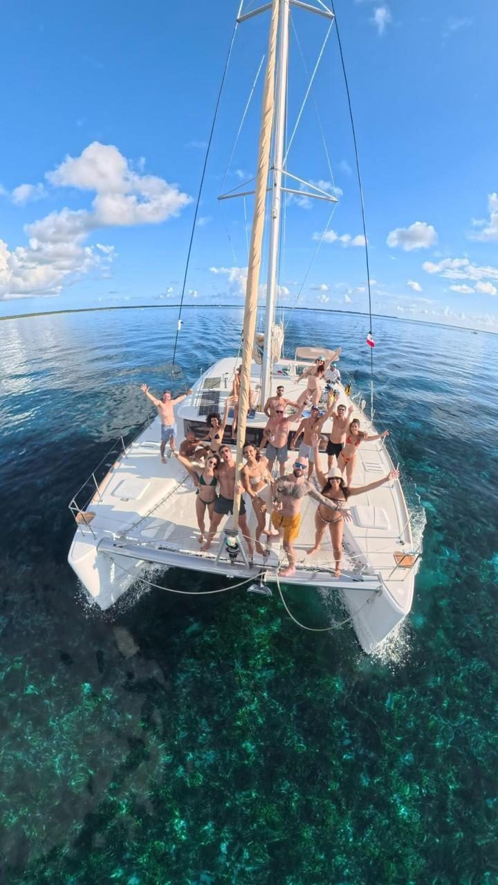 A group waving from the bow of the catamaran over the reef