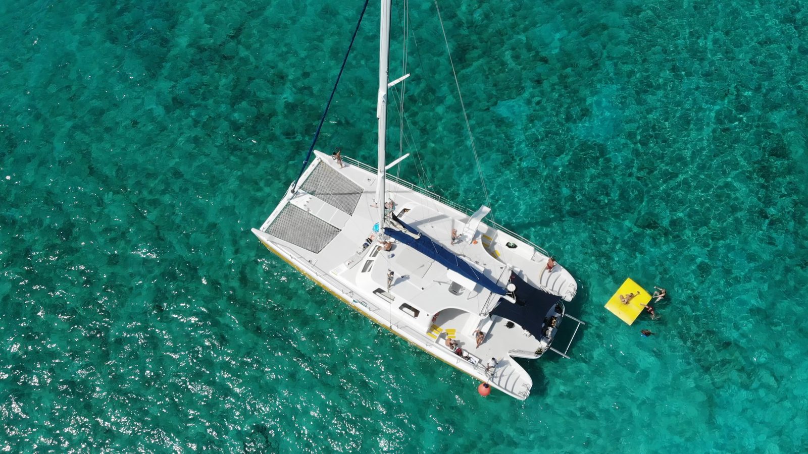 The 65-foot catamaran at anchor over turquoise water, seen from directly above, with a floating mat alongside