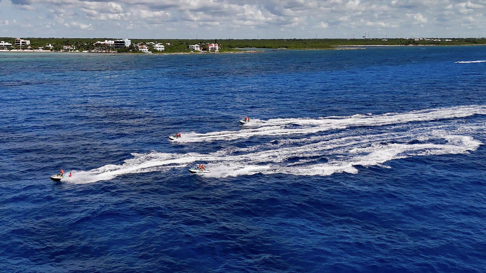 Jet skis cruising in line along the Caribbean coast, the beach behind them