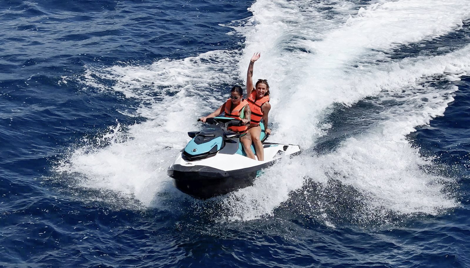 Two riders on one jet ski, waving as they carve through the spray
