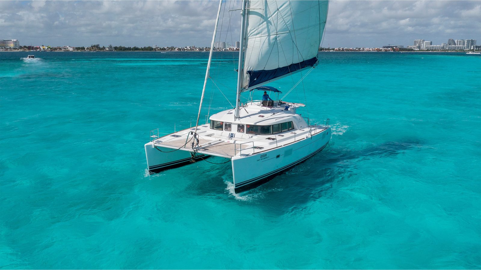 Quidam sailing over turquoise shallows, seen from the bow quarter