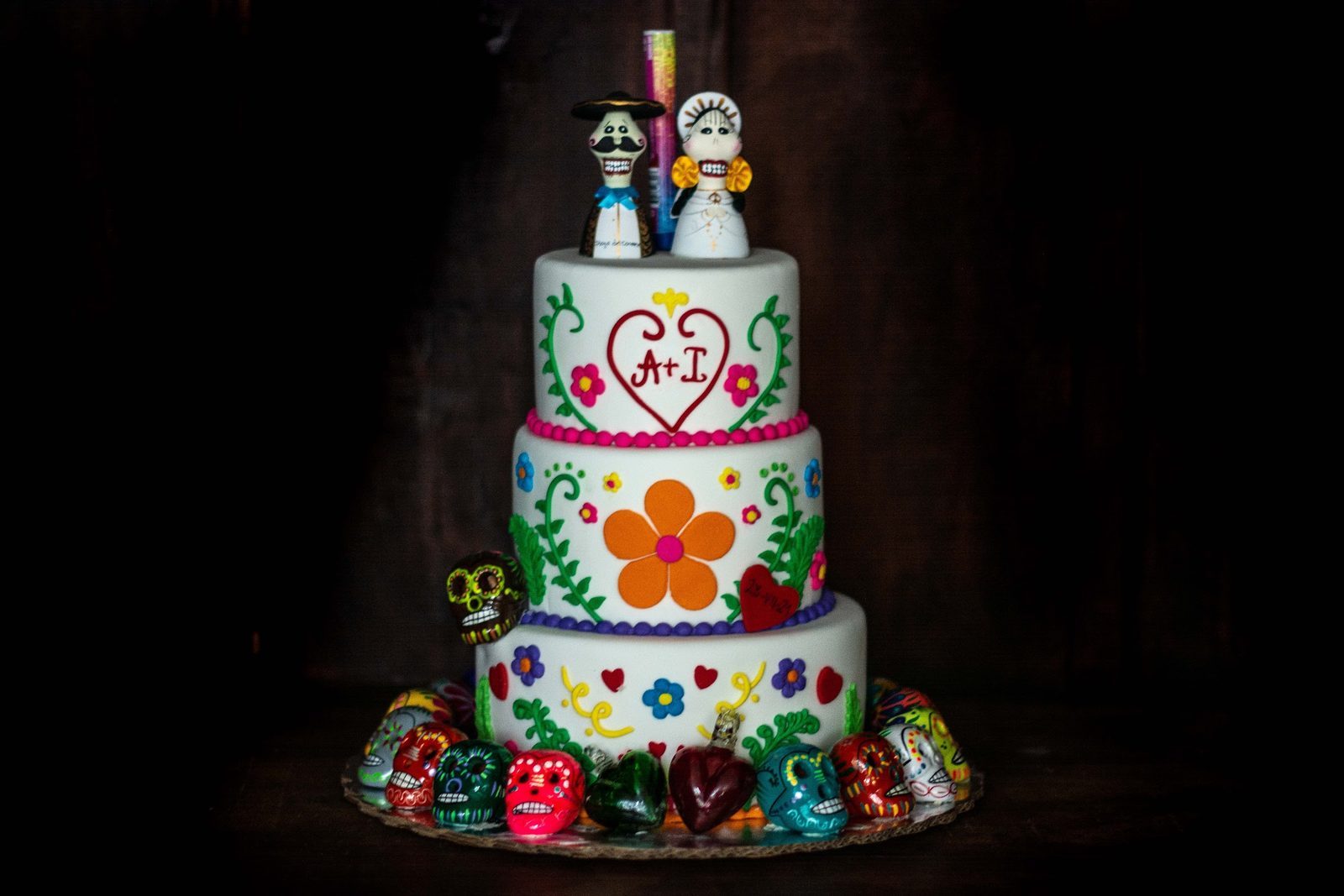 A three-tier Day of the Dead wedding cake with sugar skulls and a catrina couple on top