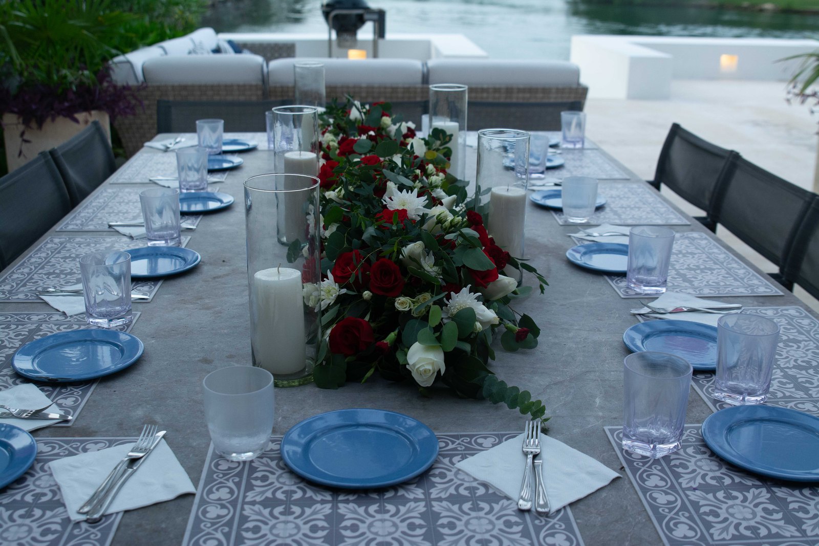 A long table dressed with a full arrangement of red and white flowers by the pool