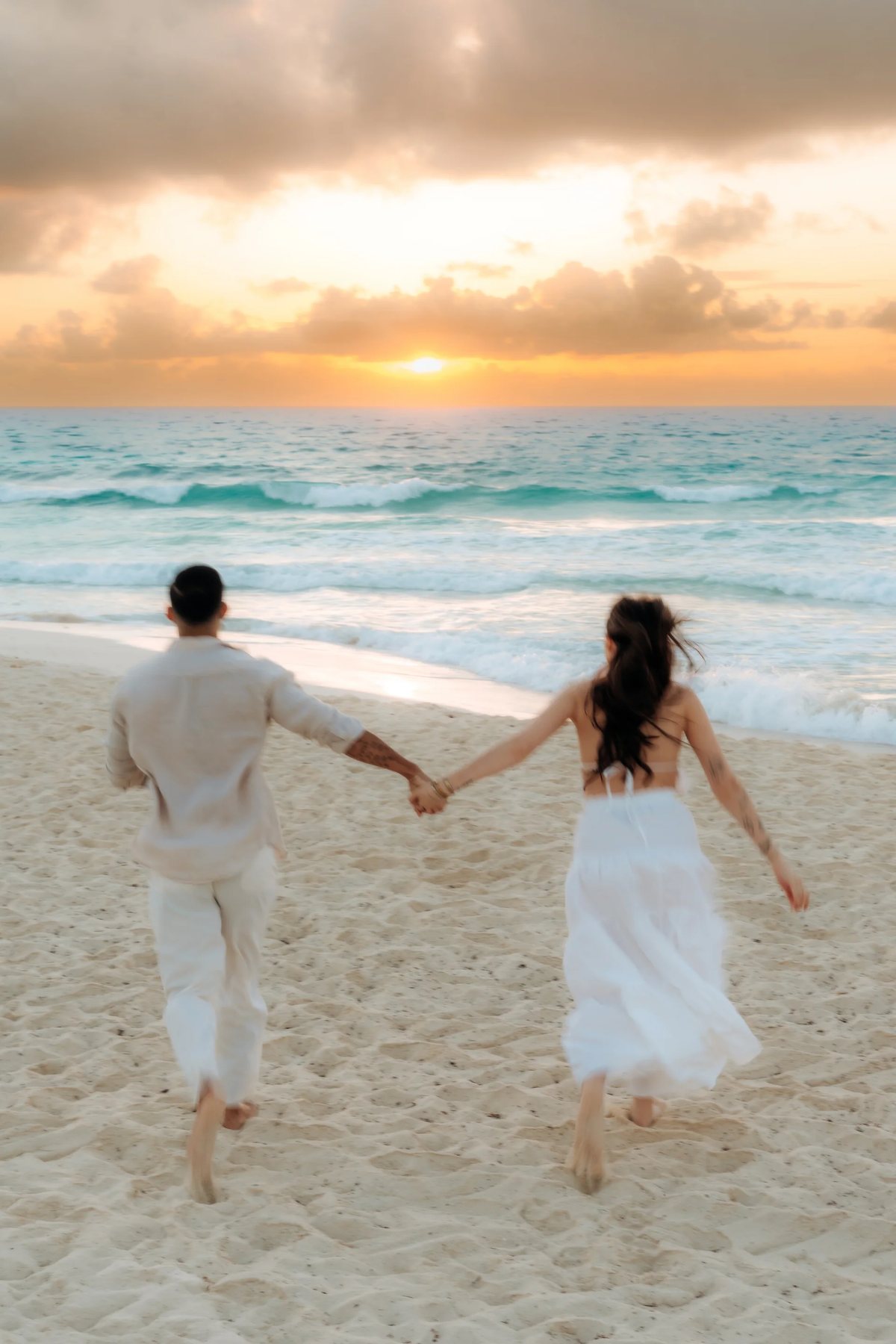 A couple running hand in hand toward the sea at sunrise