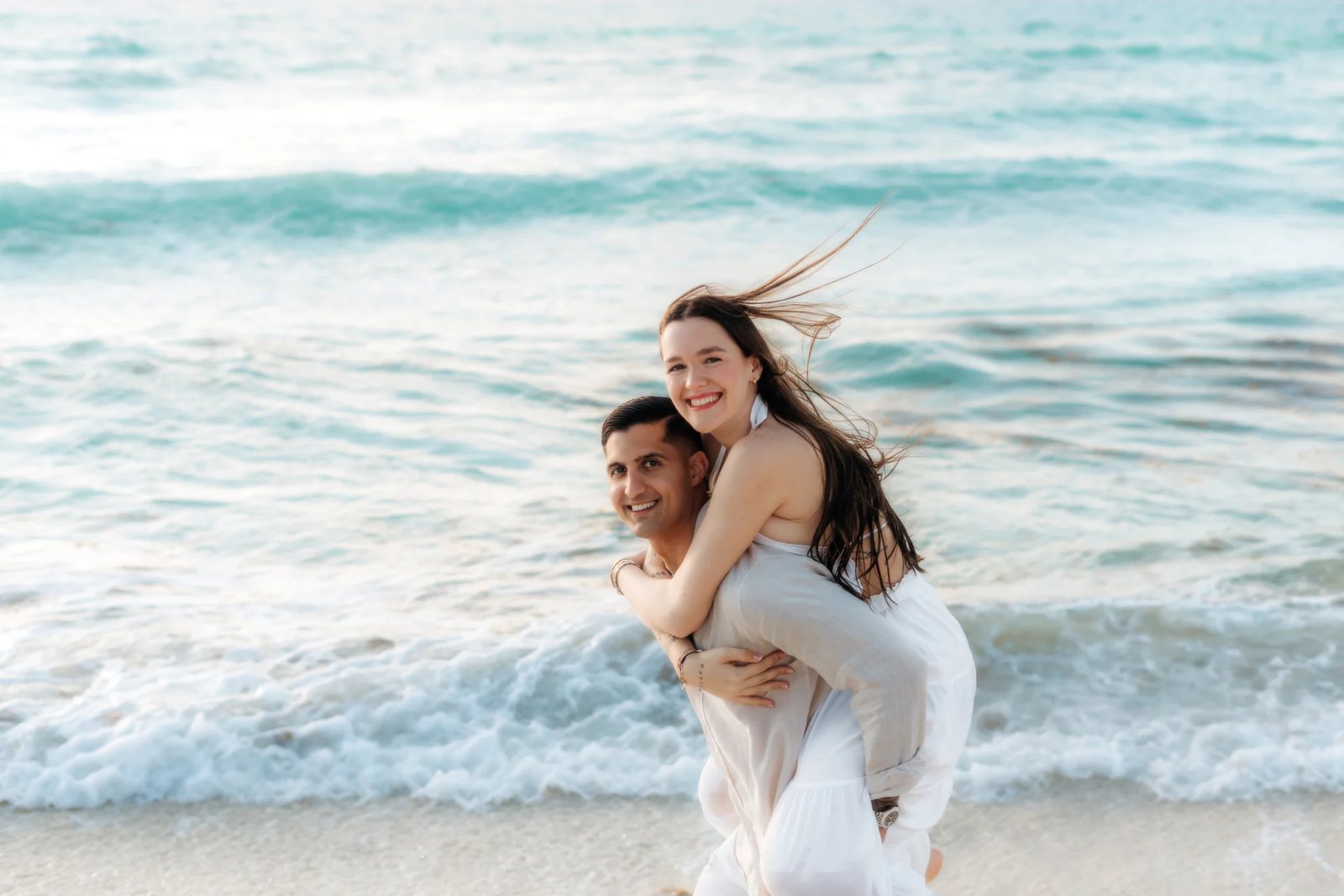 He carries her piggyback at the edge of the waves