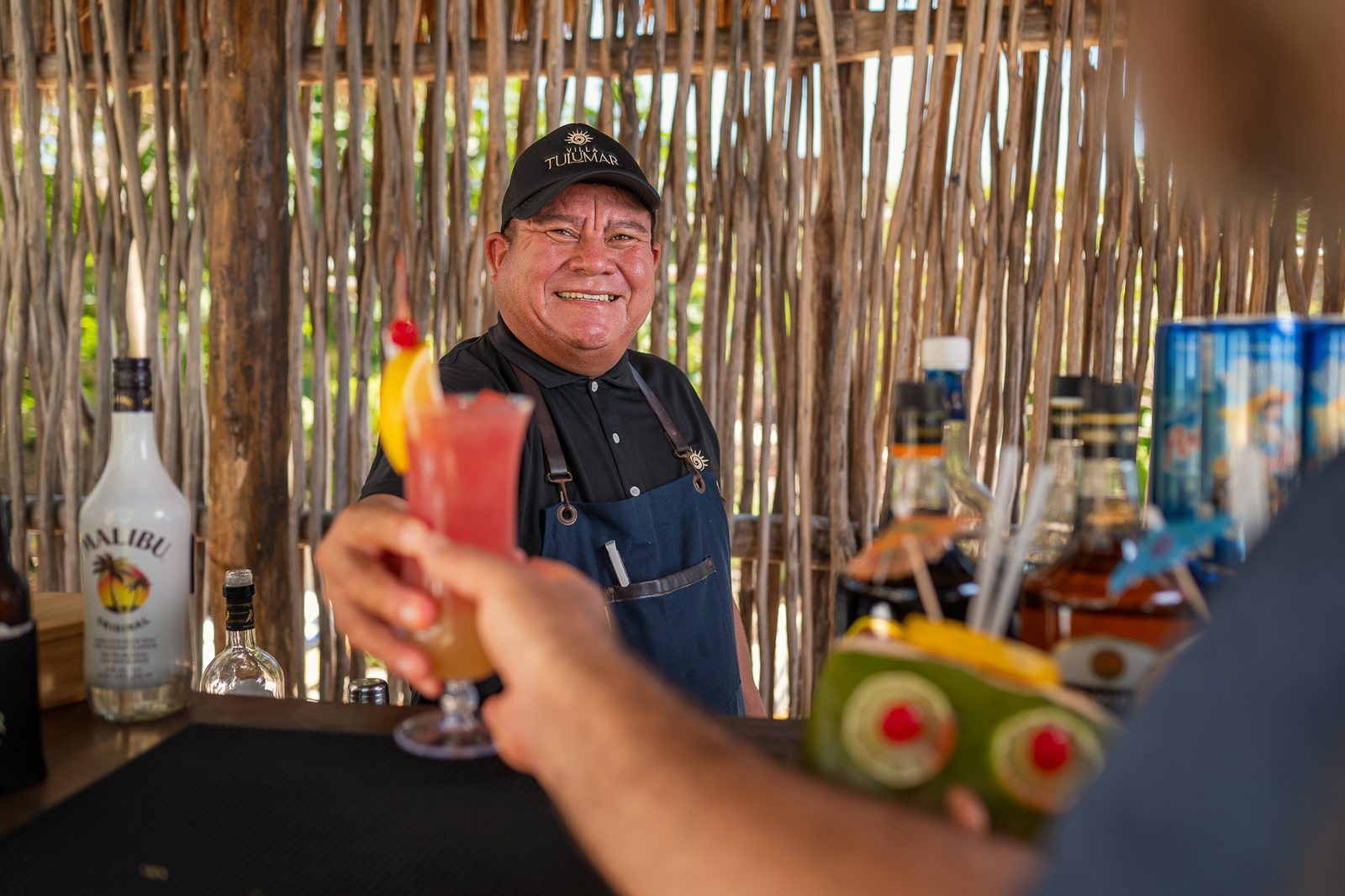 Un bartender entrega un coctel a un huésped en la barra de palapa de la villa