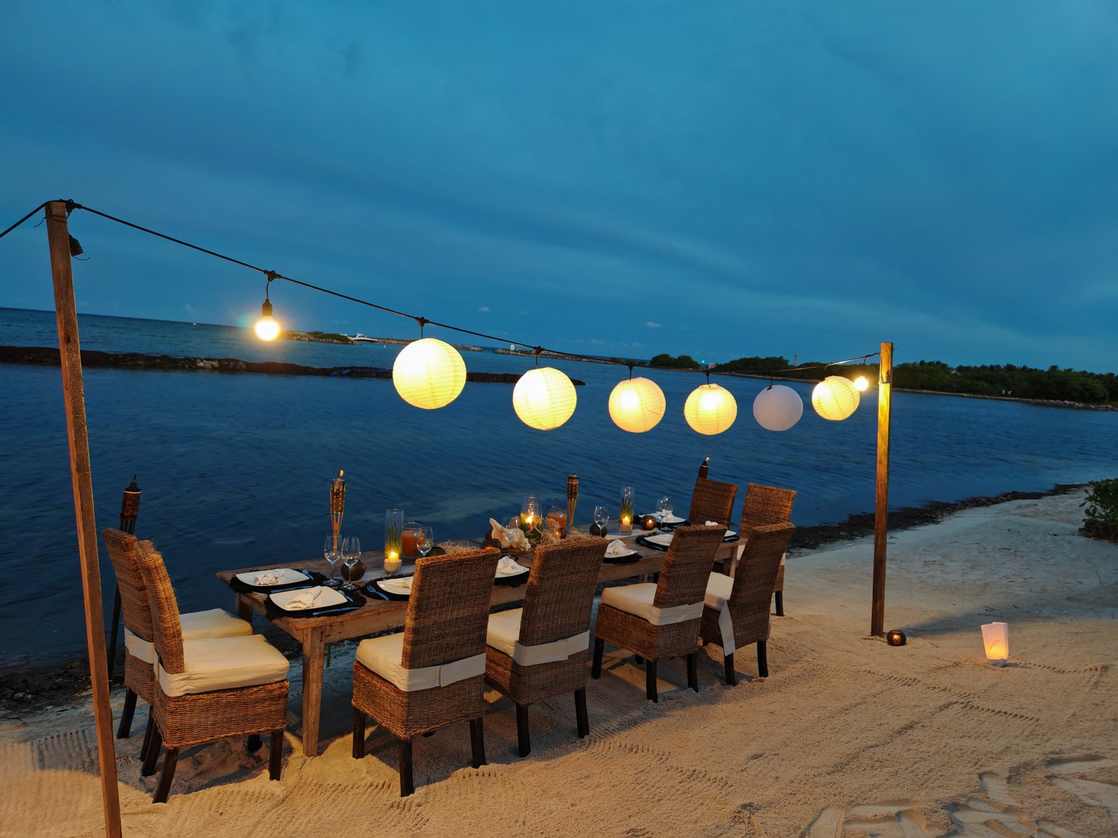 A dinner table on the sand, lit with paper lanterns