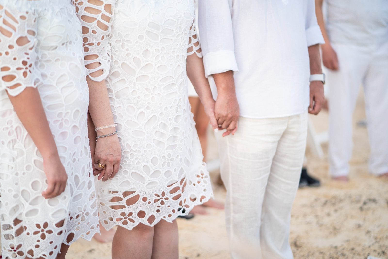 A couple dressed in white holding hands on the beach