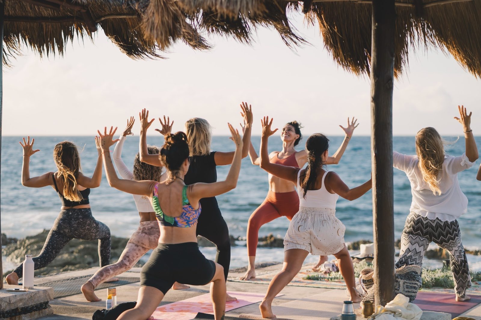 A group practicing yoga under a palapa by the sea