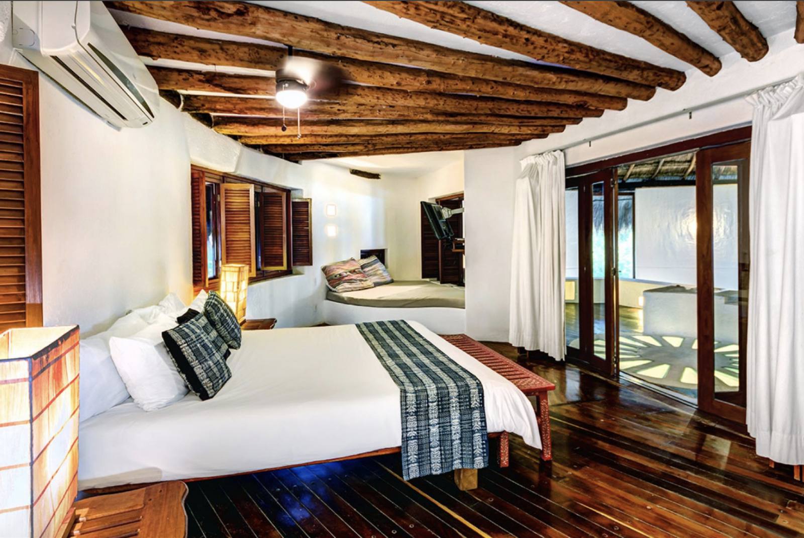 A bedroom with wooden beams and doors to the terrace