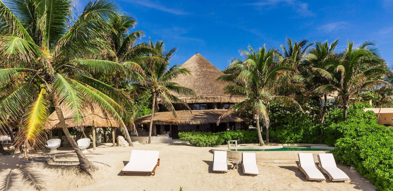 The palapa house among palms, with loungers on the sand