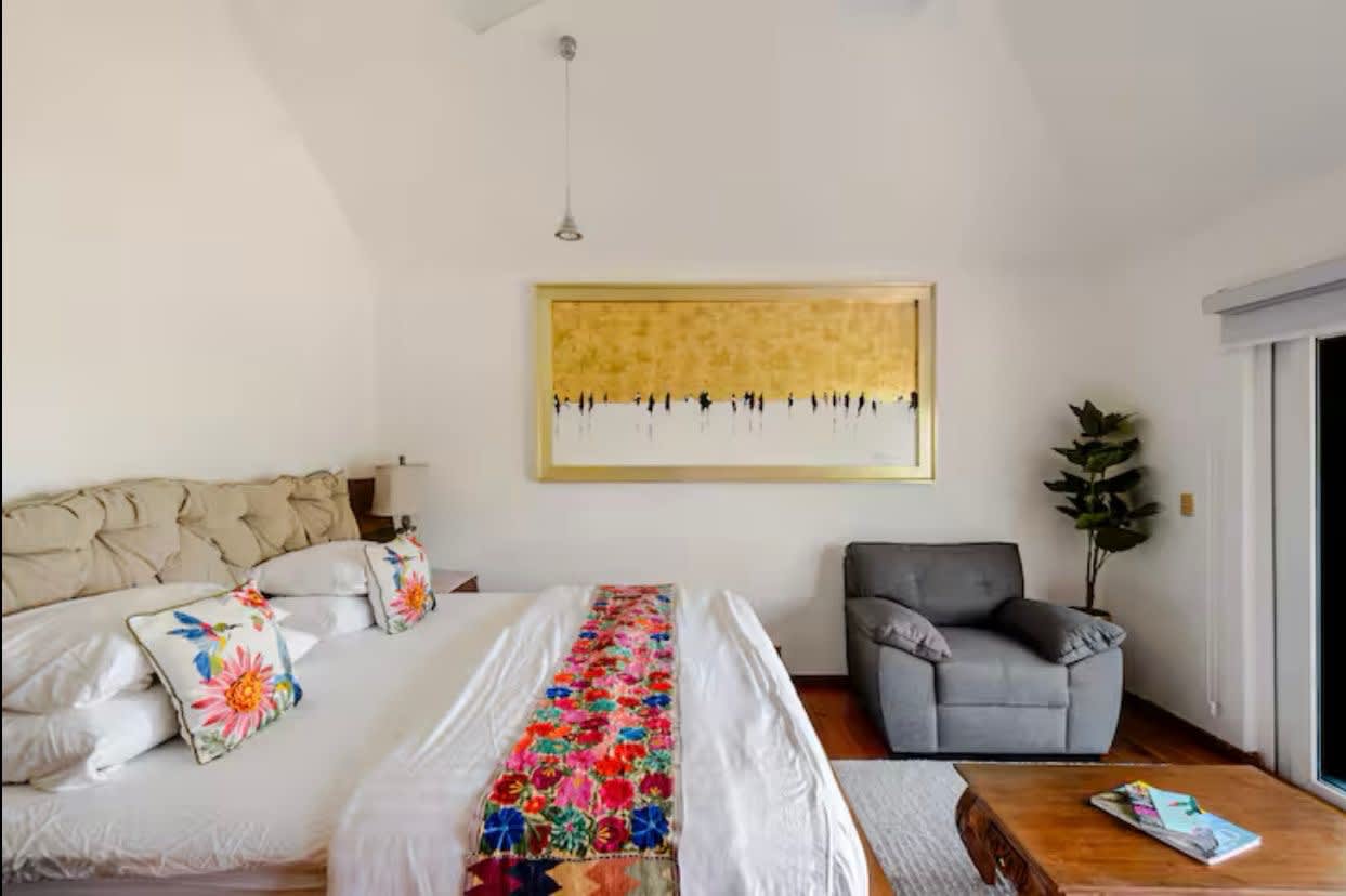 A bedroom with an embroidered runner and an armchair