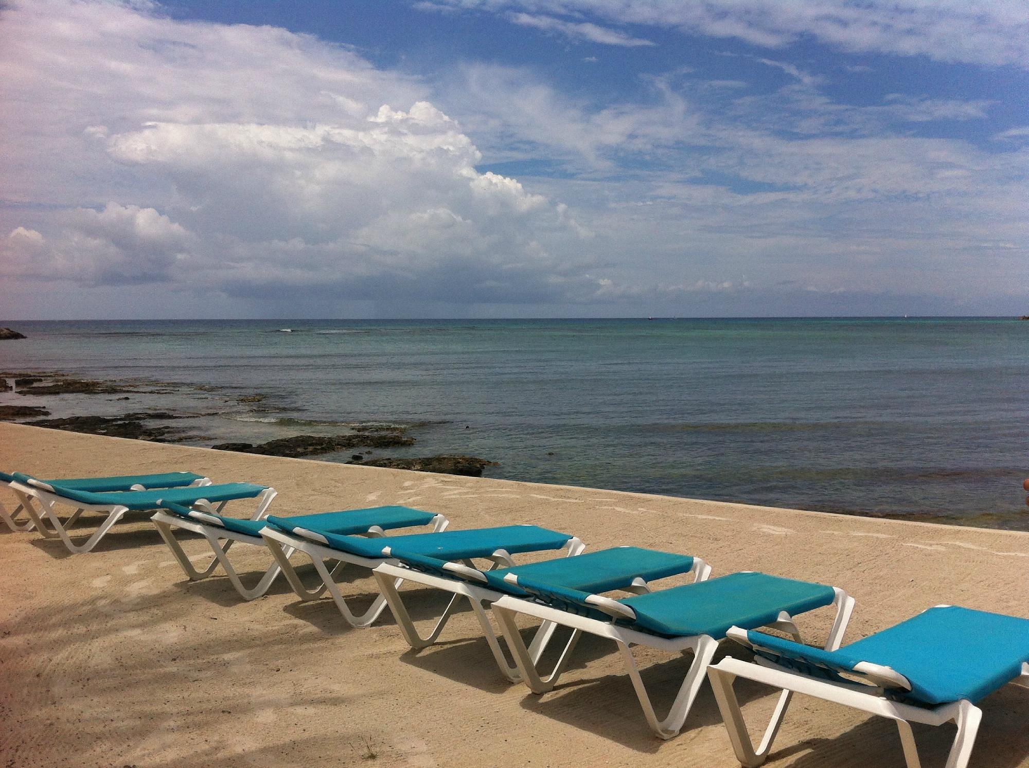 Sun loungers lined up on the beach in front of the building, facing the calm bay