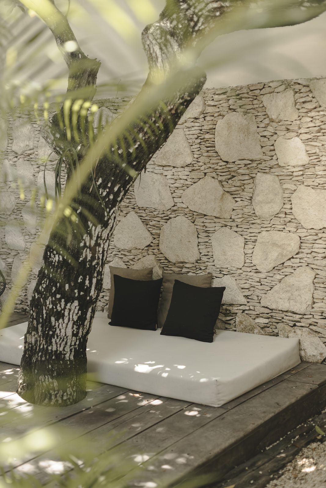 A daybed under a tree against the stone wall