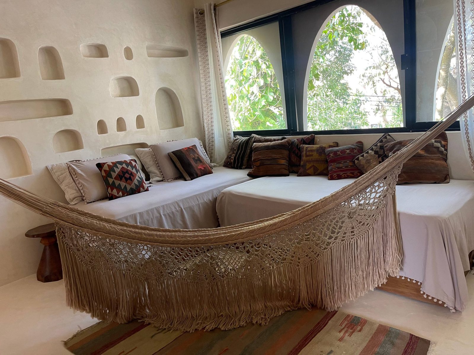 A bedroom with a hammock and arched windows to the trees