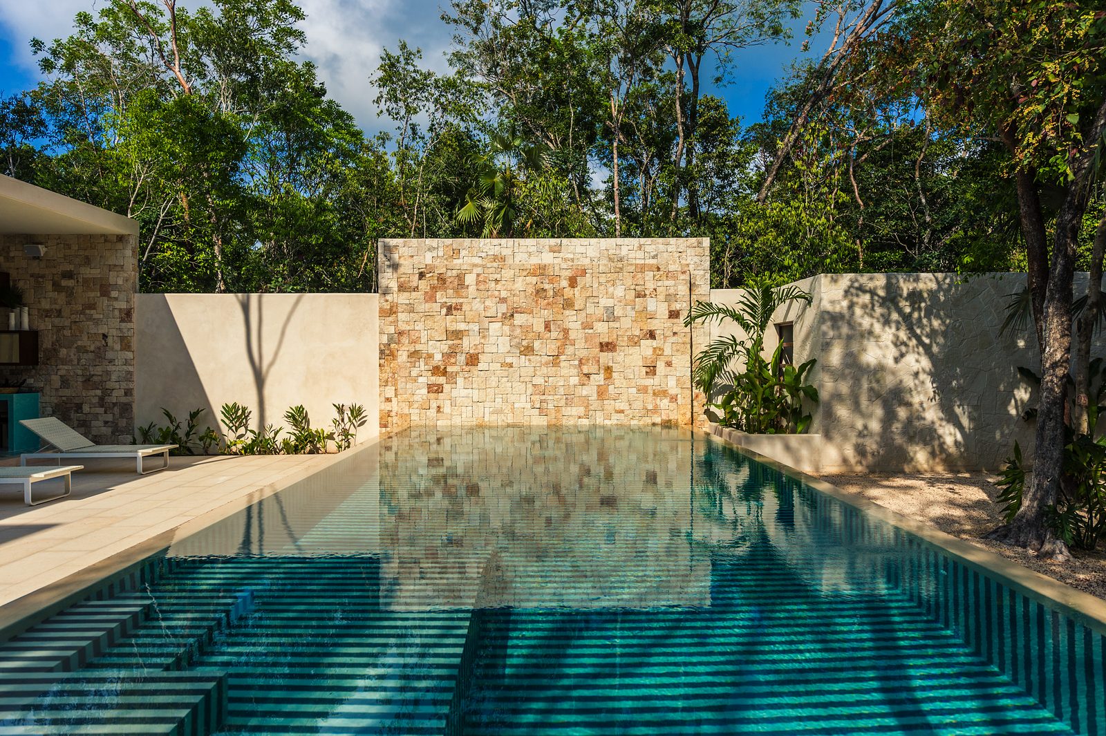 The pool reflecting a stone wall, framed by tropical gardens