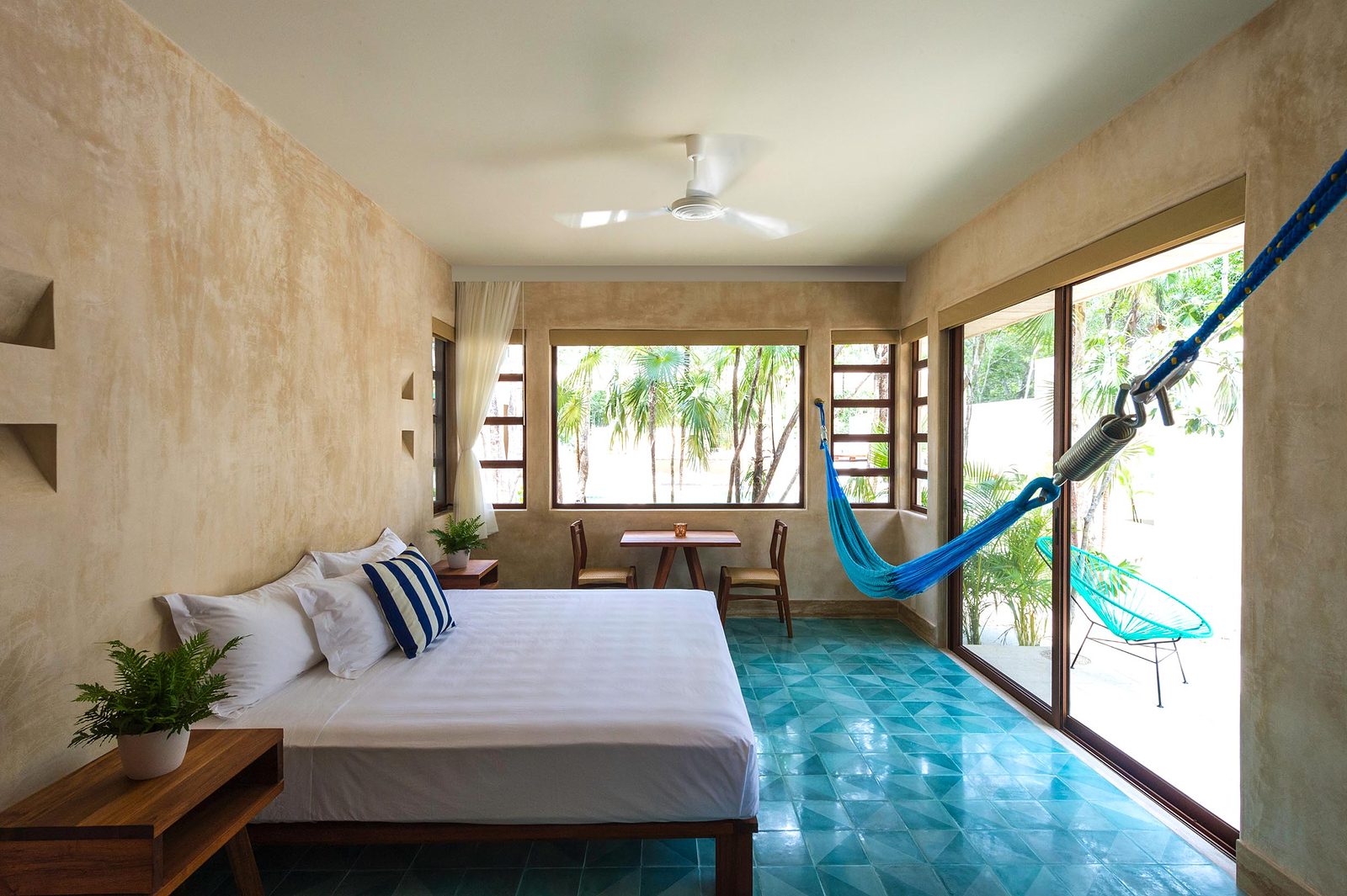 A bedroom with a king bed, a hammock and a turquoise tile floor, open to the garden