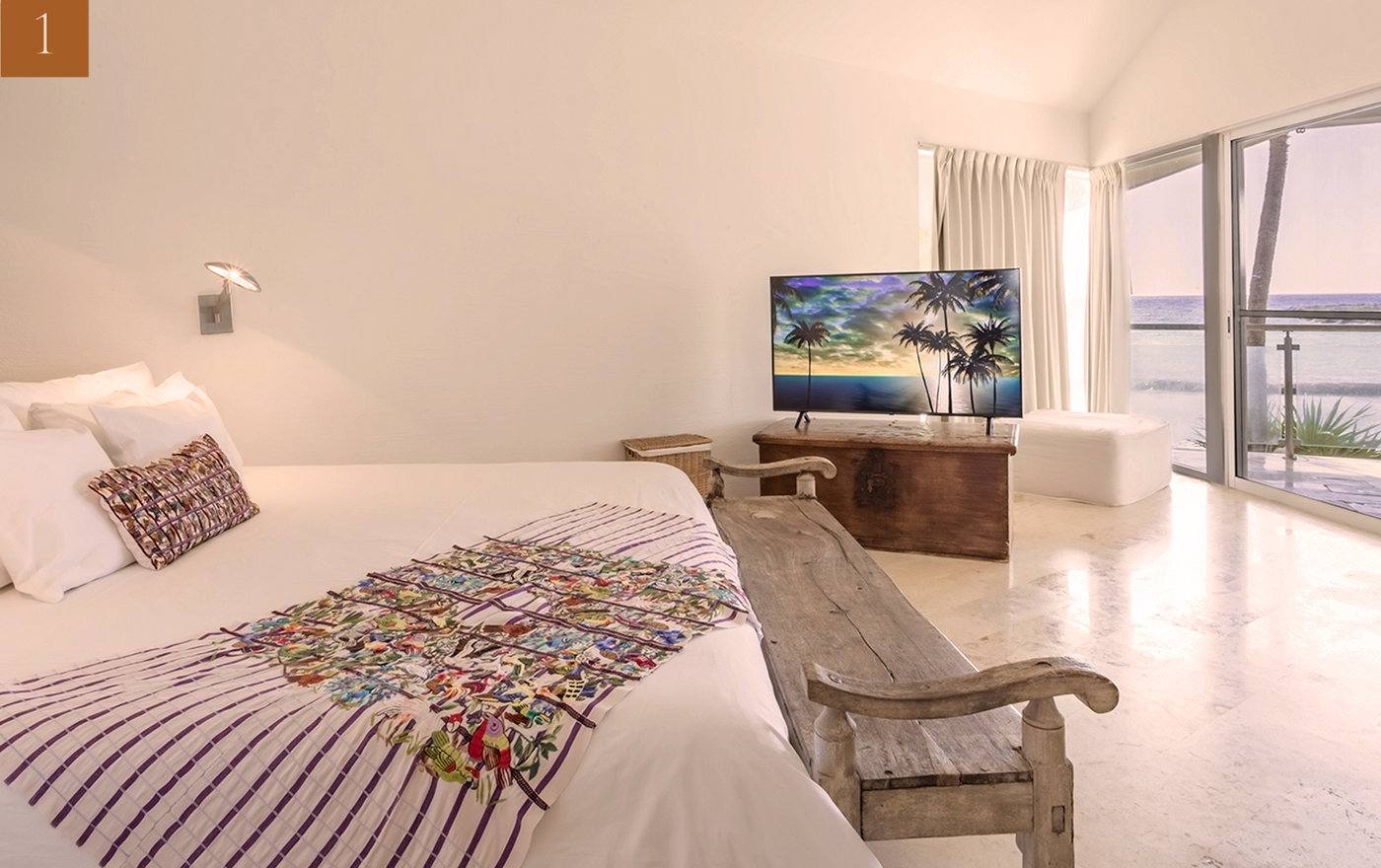 A bedroom with an embroidered throw and glass doors to the sea