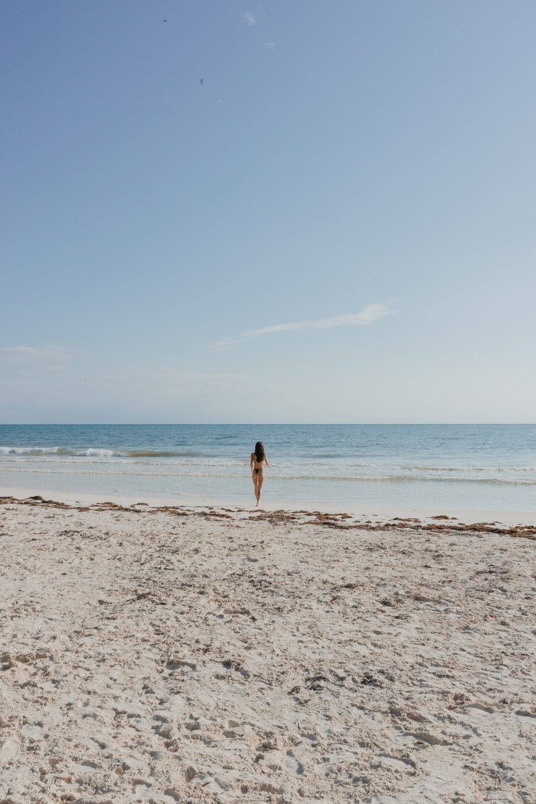 A guest walking into the sea on a wide, empty beach