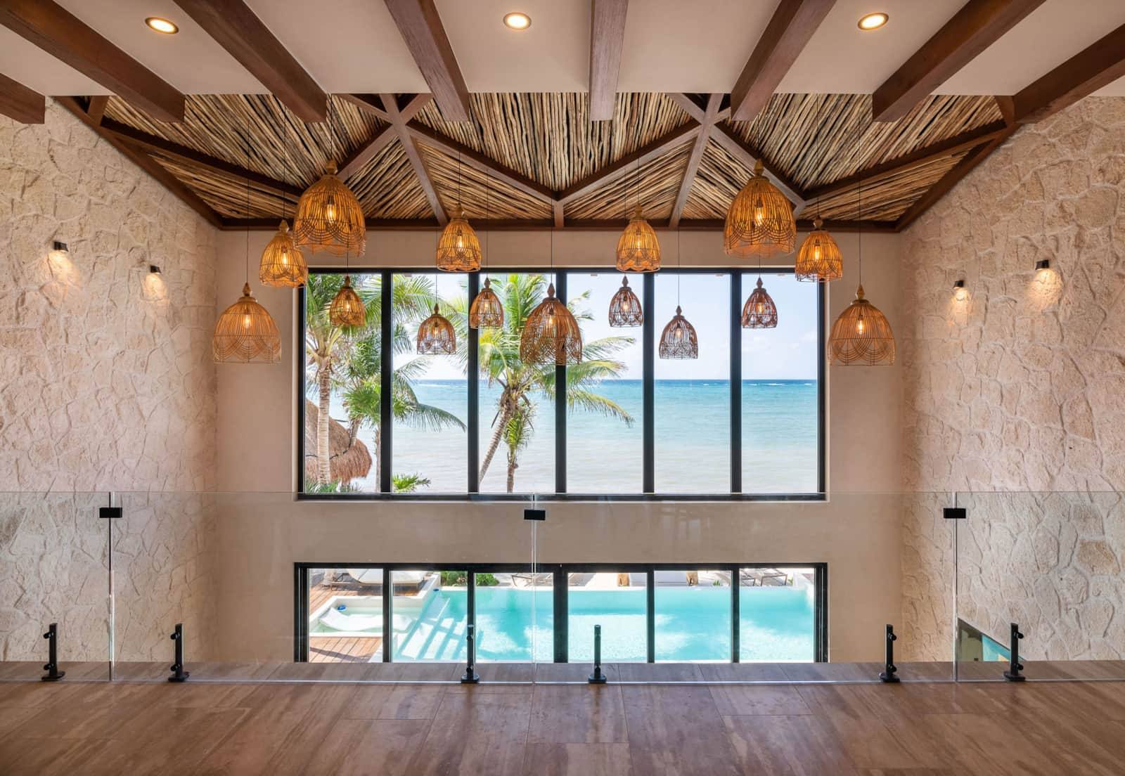 The double-height hall with woven lamps, looking out to the pool and sea